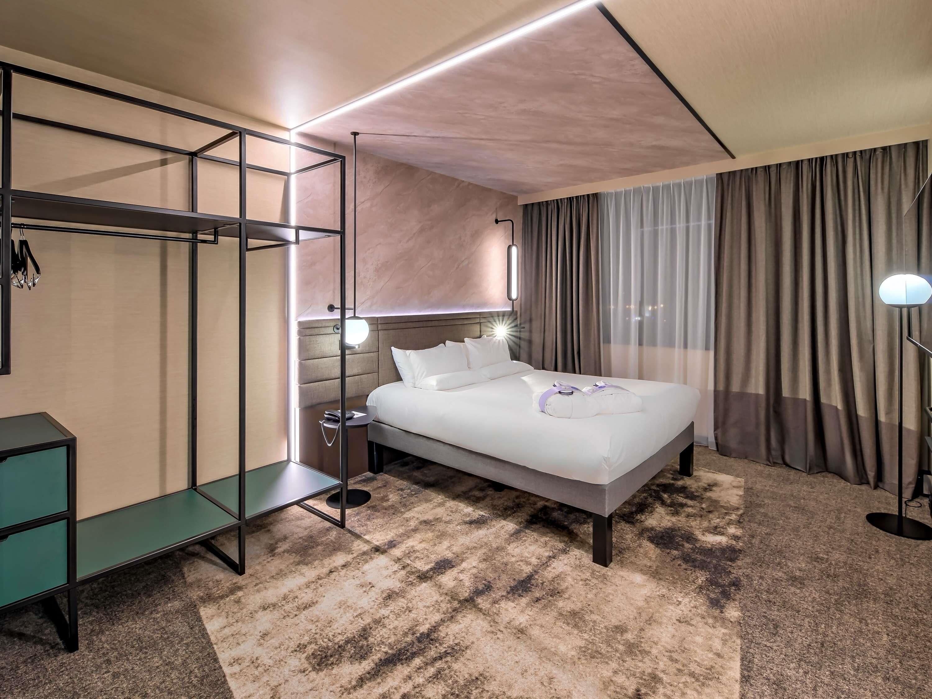 A hotel room with a bed, bedside table, lamp, and a wardrobe.