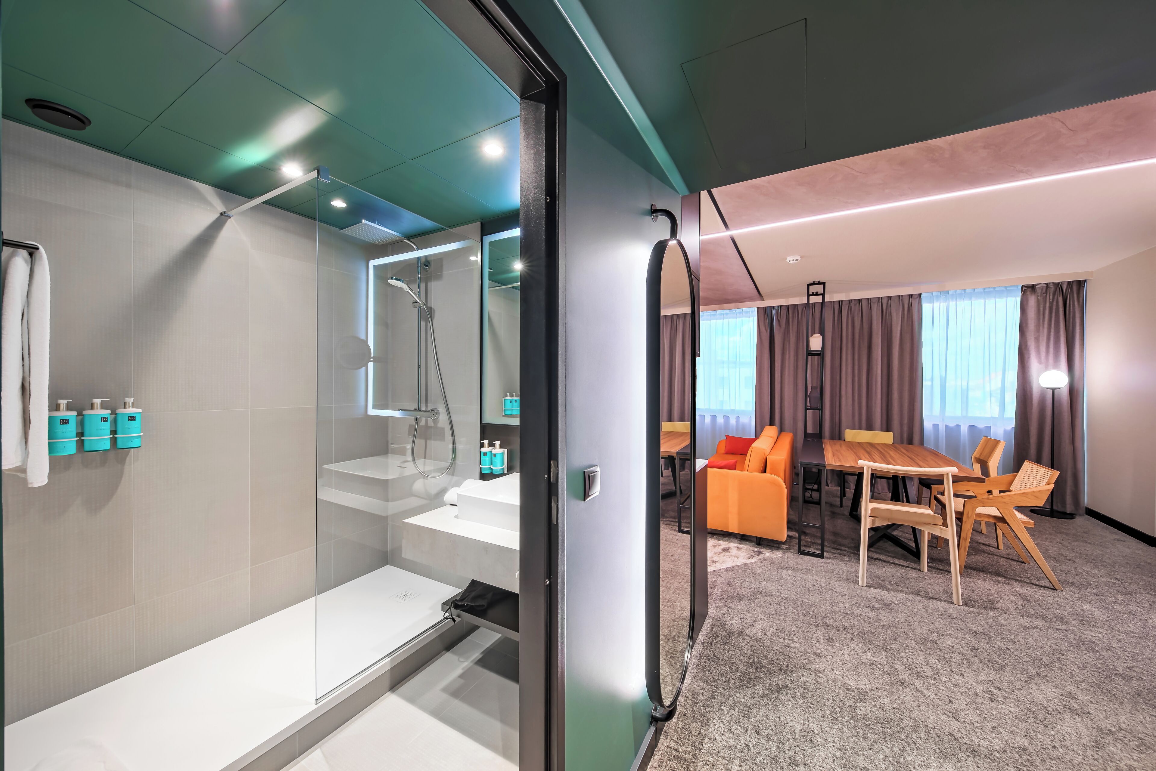 Habitación de hotel moderna con cabina de ducha de vidrio, bañera blanca, zona de comedor con mesa y sillas, y suelo alfombrado.
