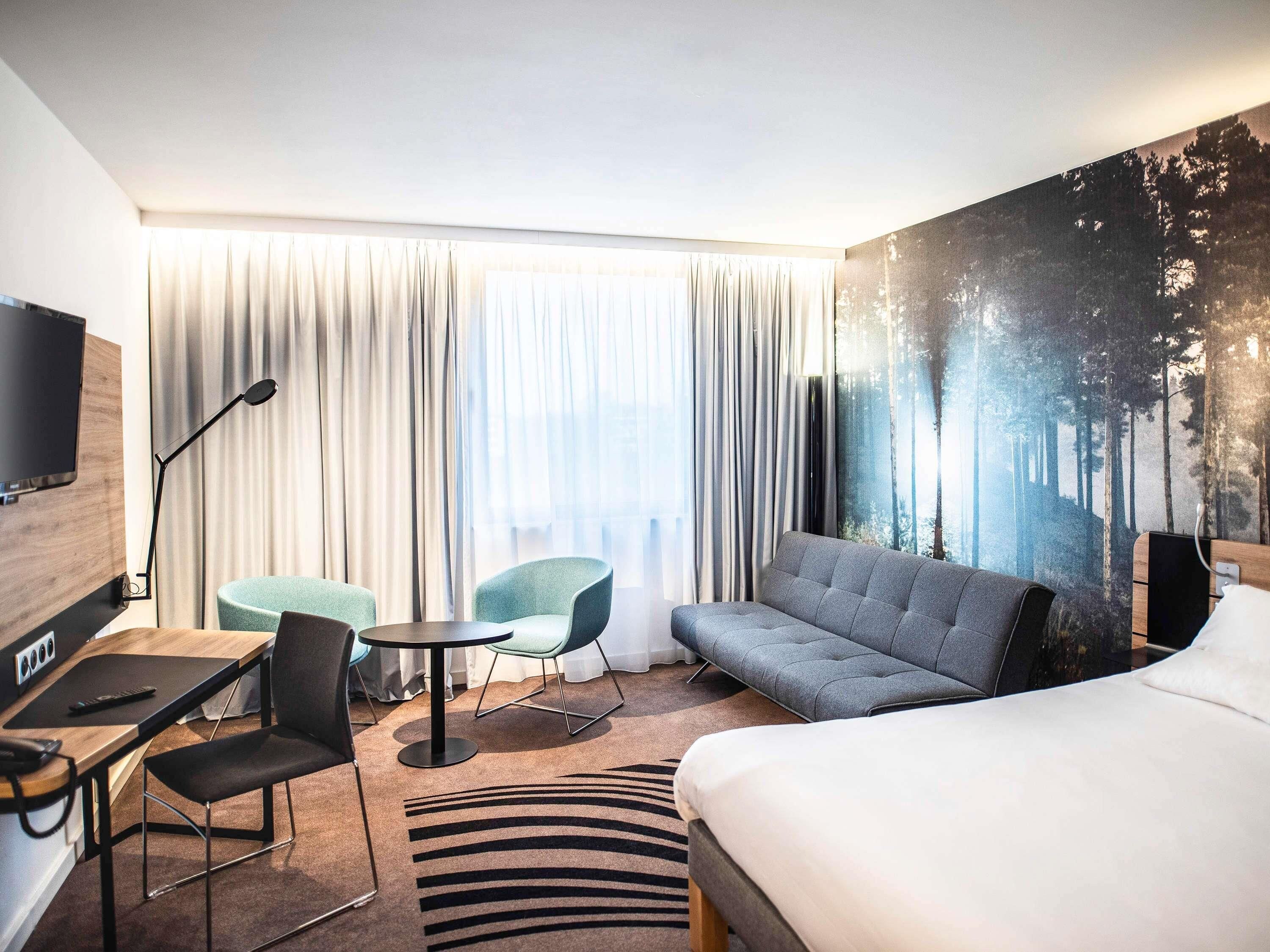 Habitación de hotel con cama, sofá, escritorio con silla, una mesita y televisión.
