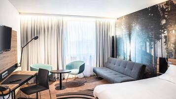 Habitación de hotel con cama, sofá, escritorio con silla, una mesita y televisión.