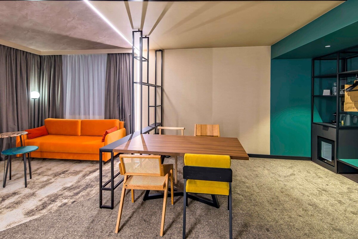 A modern room with a sofa, dining table, chairs, and a bookshelf.