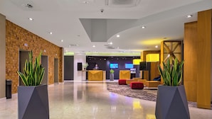 A modern lobby with a brick wall, two large planters with green plants, a reception desk, and a seating area with red chairs. - Novotel Krakow Centrum (Kraków)