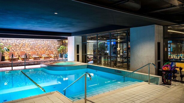 An indoor swimming pool with a stone wall, lounge chairs, and exercise equipment. - Novotel Krakow Centrum (Kraków)