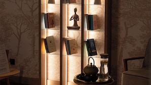 A cozy reading area with a wooden bookshelf, a small table with a teapot, and a chair. - Novotel Krakow Centrum (Kraków)