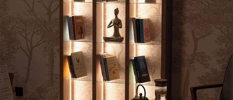 Un rincón acogedor para leer, con una estantería de madera, una mesita con tetera y un sillón.
