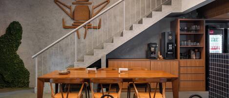 A modern dining area with a wooden table and chairs, a staircase, and a kitchen area with a refrigerator and cabinets.