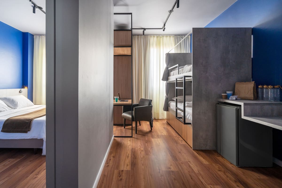 Une chambre d’hôtel de taille réduite, comprenant un lit, un bureau, une chaise, une petite kitchenette et une armoire.