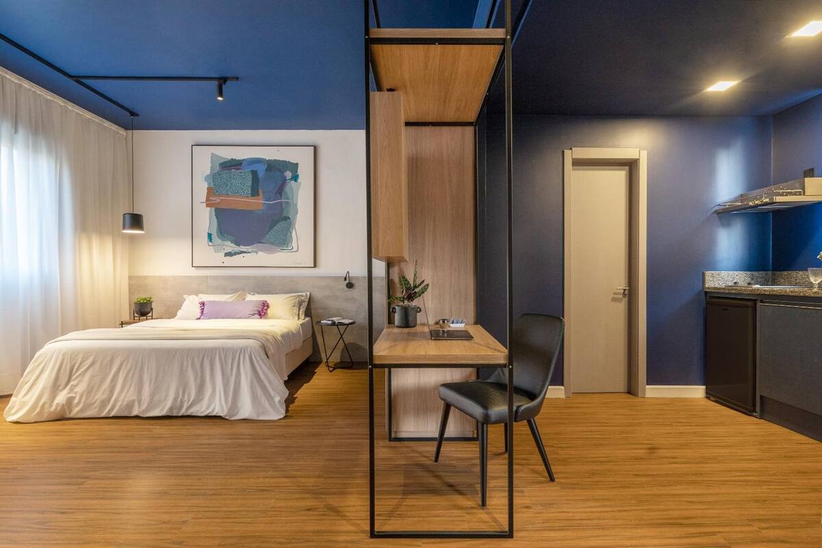 Une chambre d’hôtel moderne équipée d’un lit, d’un bureau, d’une chaise, d’une plante en pot et d’un coin cuisine.