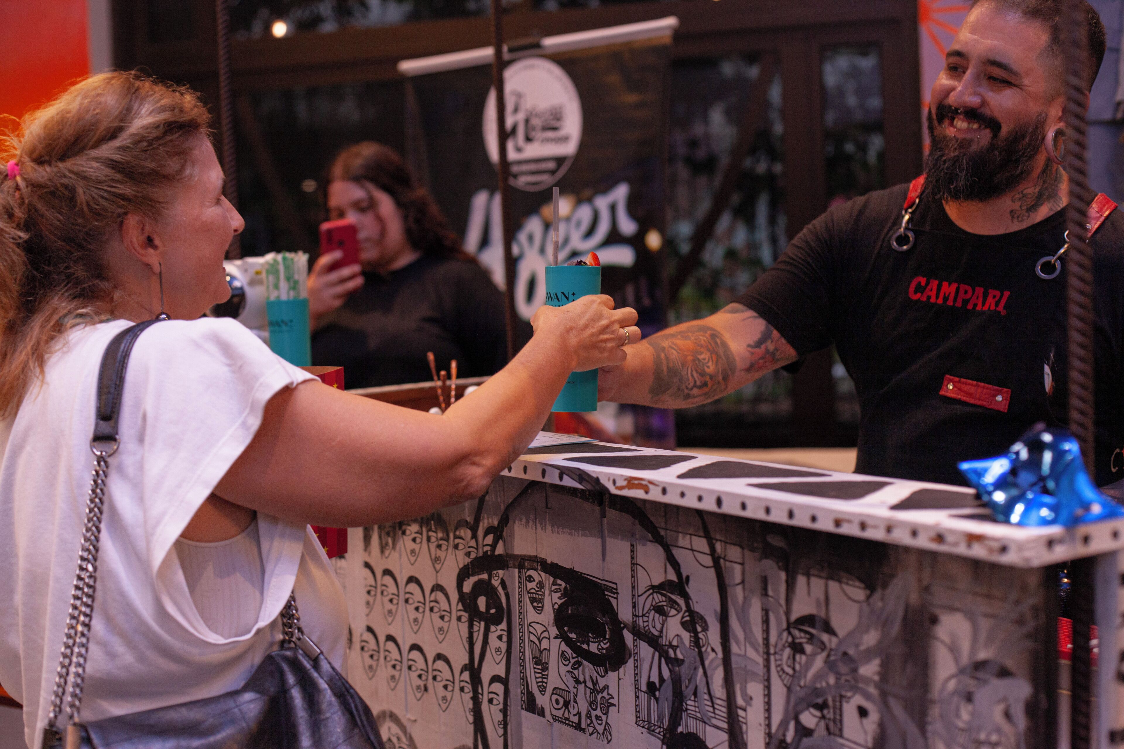A person holding a drink at a counter with a wall featuring various drawings.