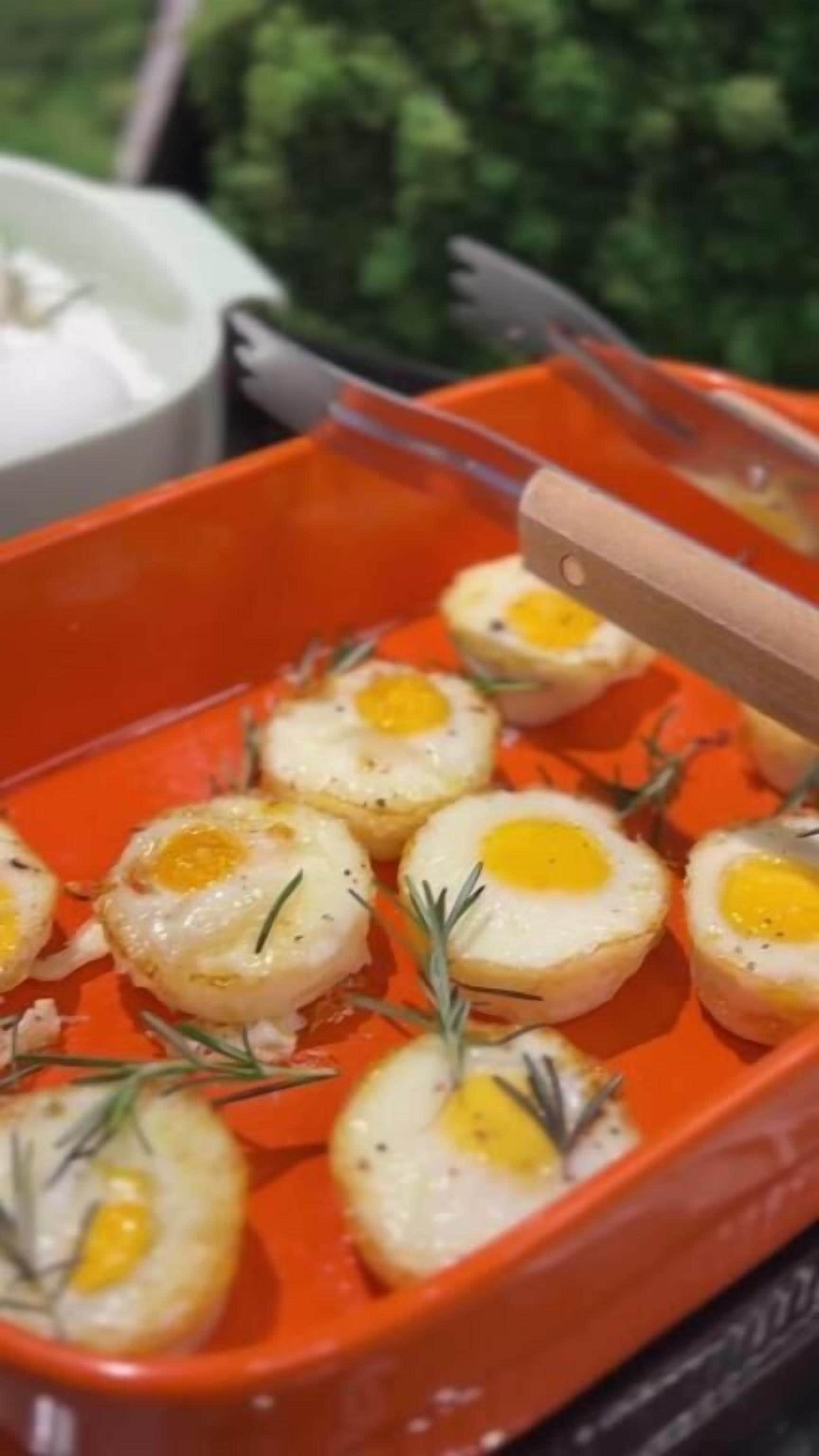 A tray of poached eggs garnished with rosemary, served on an orange plate.