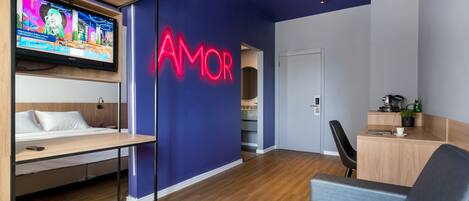 Et moderne hotelværelse med fjernsyn, et neon-skilt med teksten "AMOR", et skrivebord og en seng.