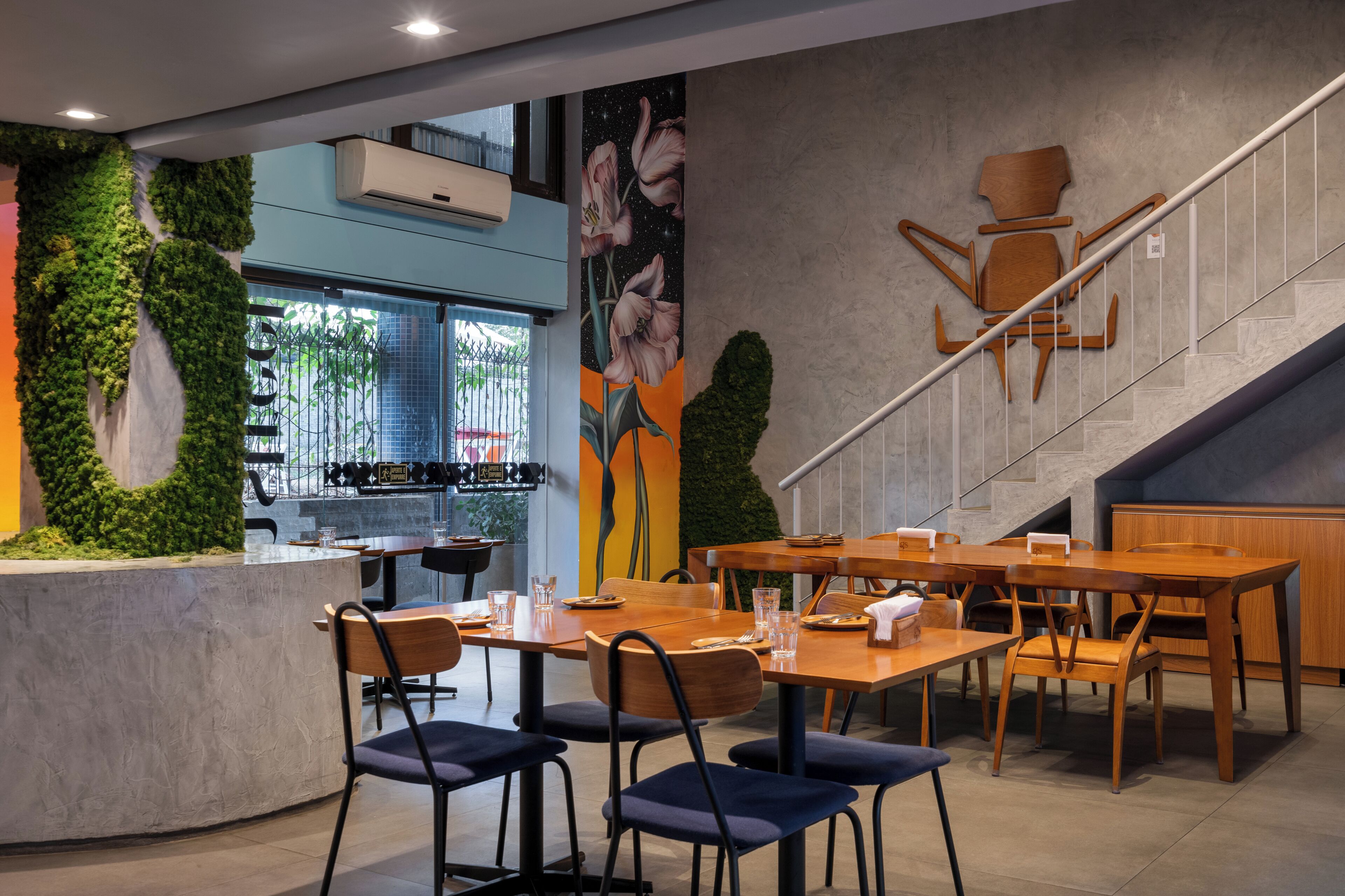 A restaurant with a staircase, wooden tables, and chairs, and a mural on the wall.