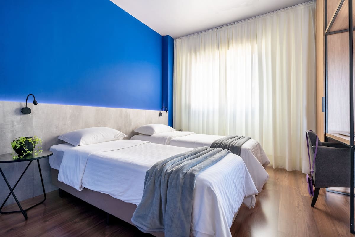 Une chambre d’hôtel avec deux lits, une petite table avec une plante et un bureau avec une chaise.