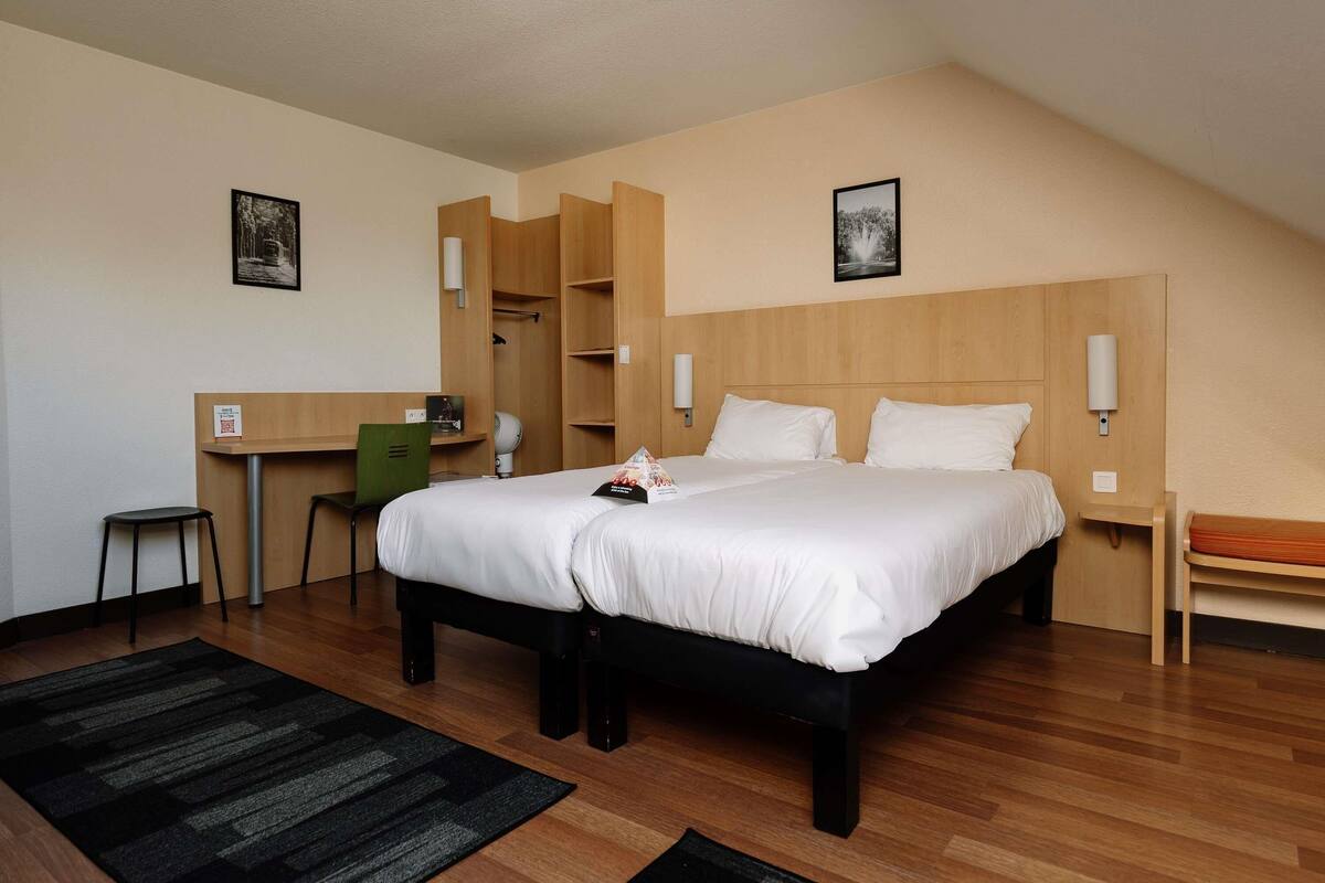 Quarto de hotel com cama grande, escrivaninha, cadeira e mesa pequena.