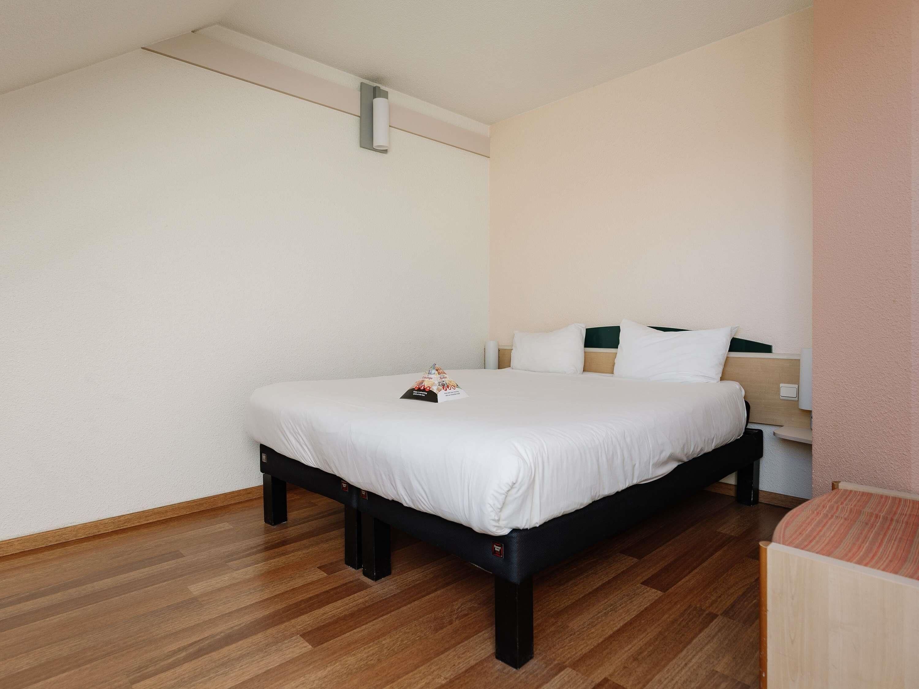 A neatly arranged hotel room with a single bed, a bedside table, and a small wooden chair.