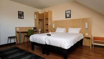 A hotel room with a large bed, a desk, a chair, and a wardrobe.
