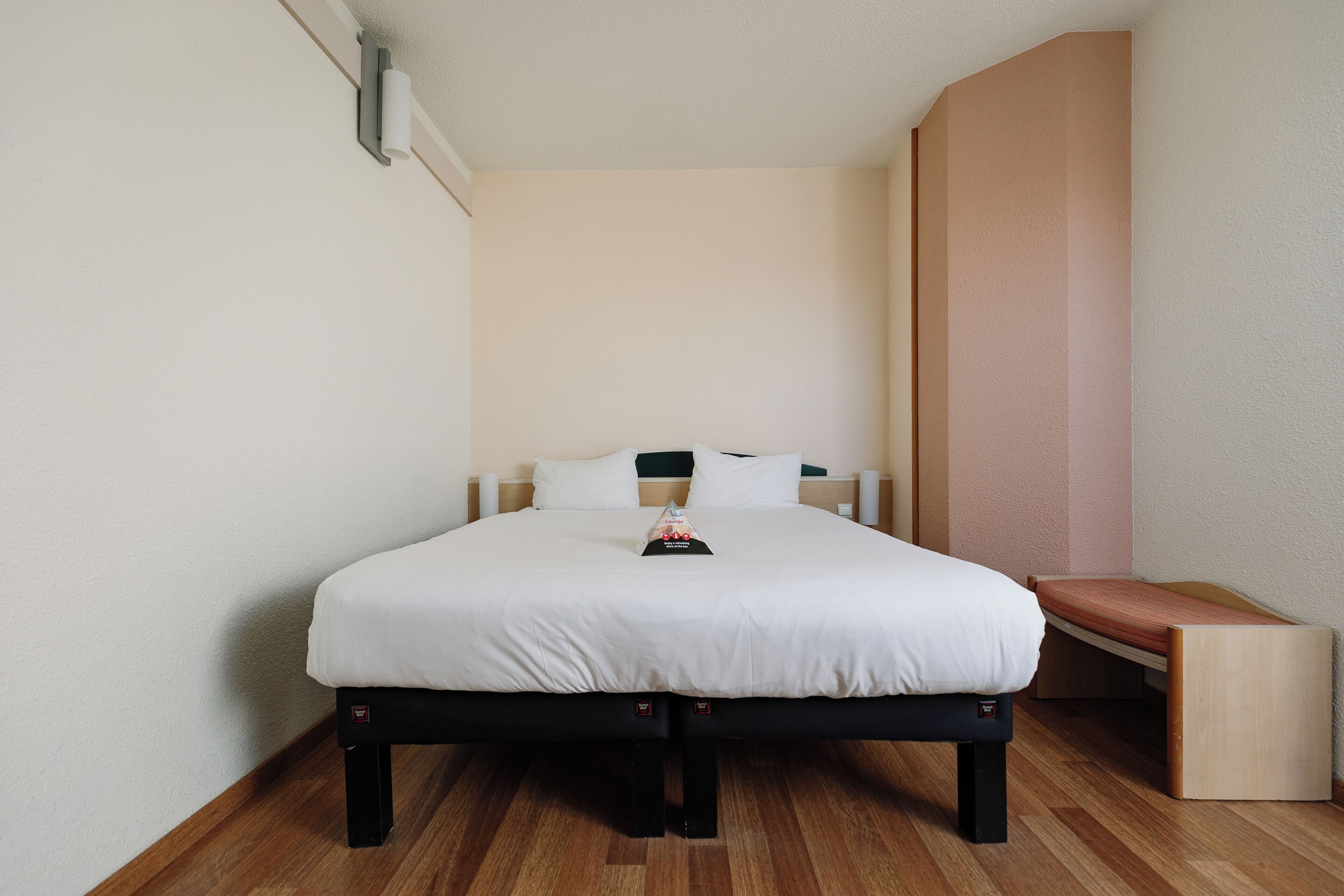 A neatly arranged hotel room with a bed, a bench, and a small table.