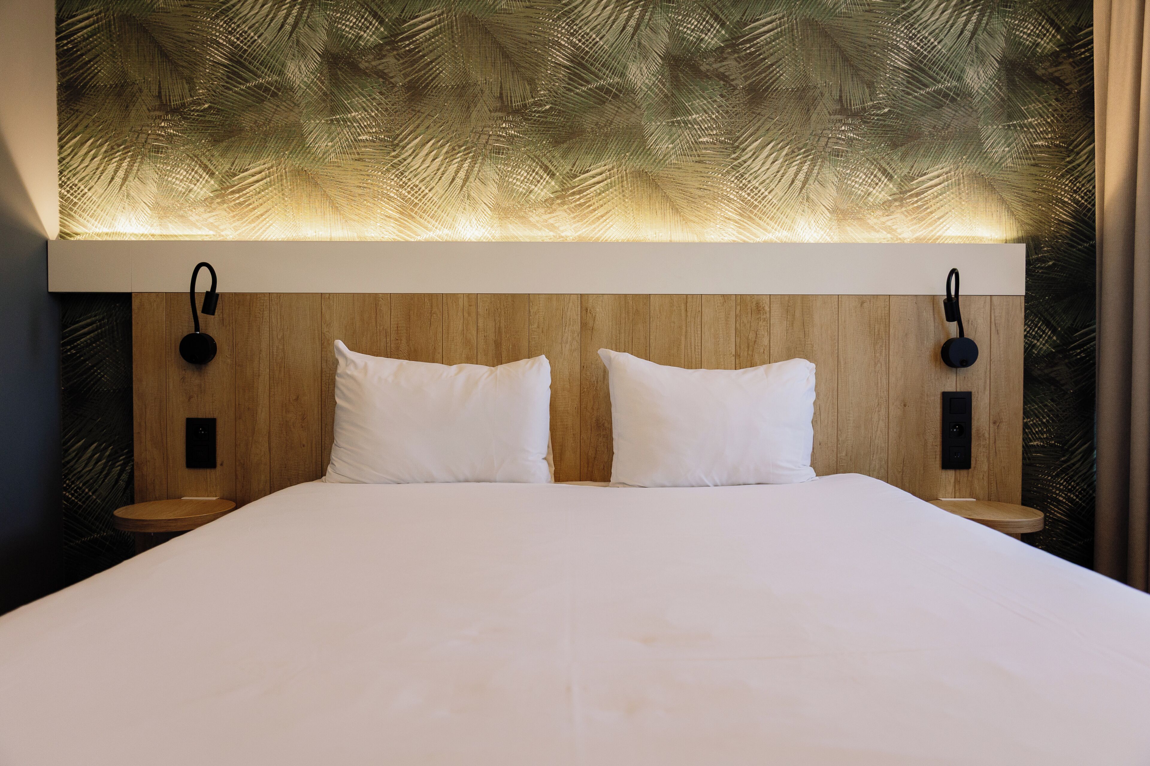 A hotel room with a large bed, wooden headboard, and two bedside tables with lamps.