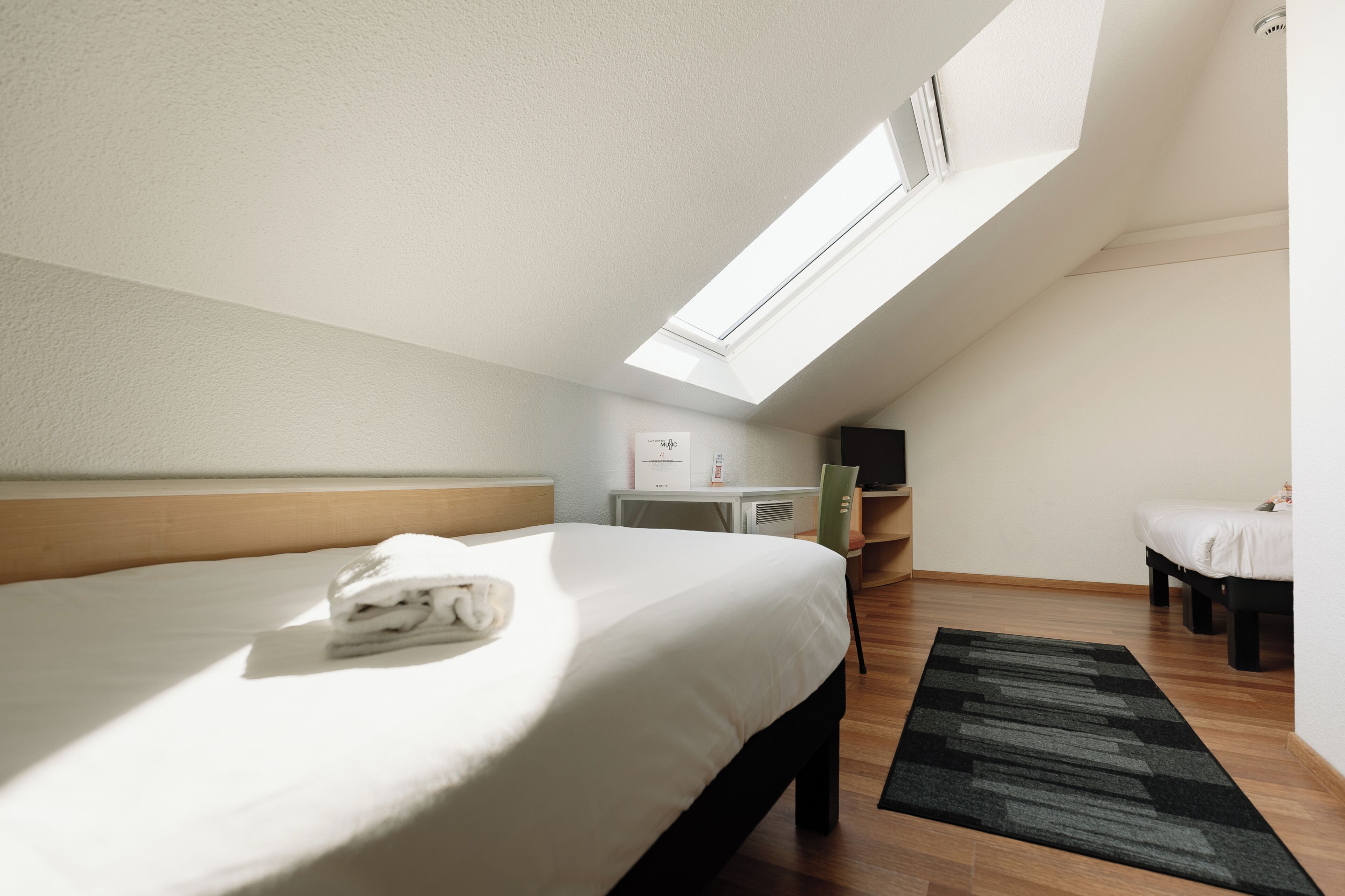 A room with a skylight, a bed, a desk, and a chair.