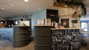 A reception area with a counter, two large barrels, a sign reading 'WELCOME @ IBIS WATERLOO,' and a menu board. - ibis Brussels Waterloo (Waterloo)