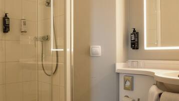 Een badkamer met een douche met glazen wand, een toilet, een wastafel met spiegel en toiletartikelen.