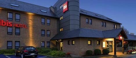 A hotel with a prominent 'ibis' sign, a parking lot, and a building with multiple windows.