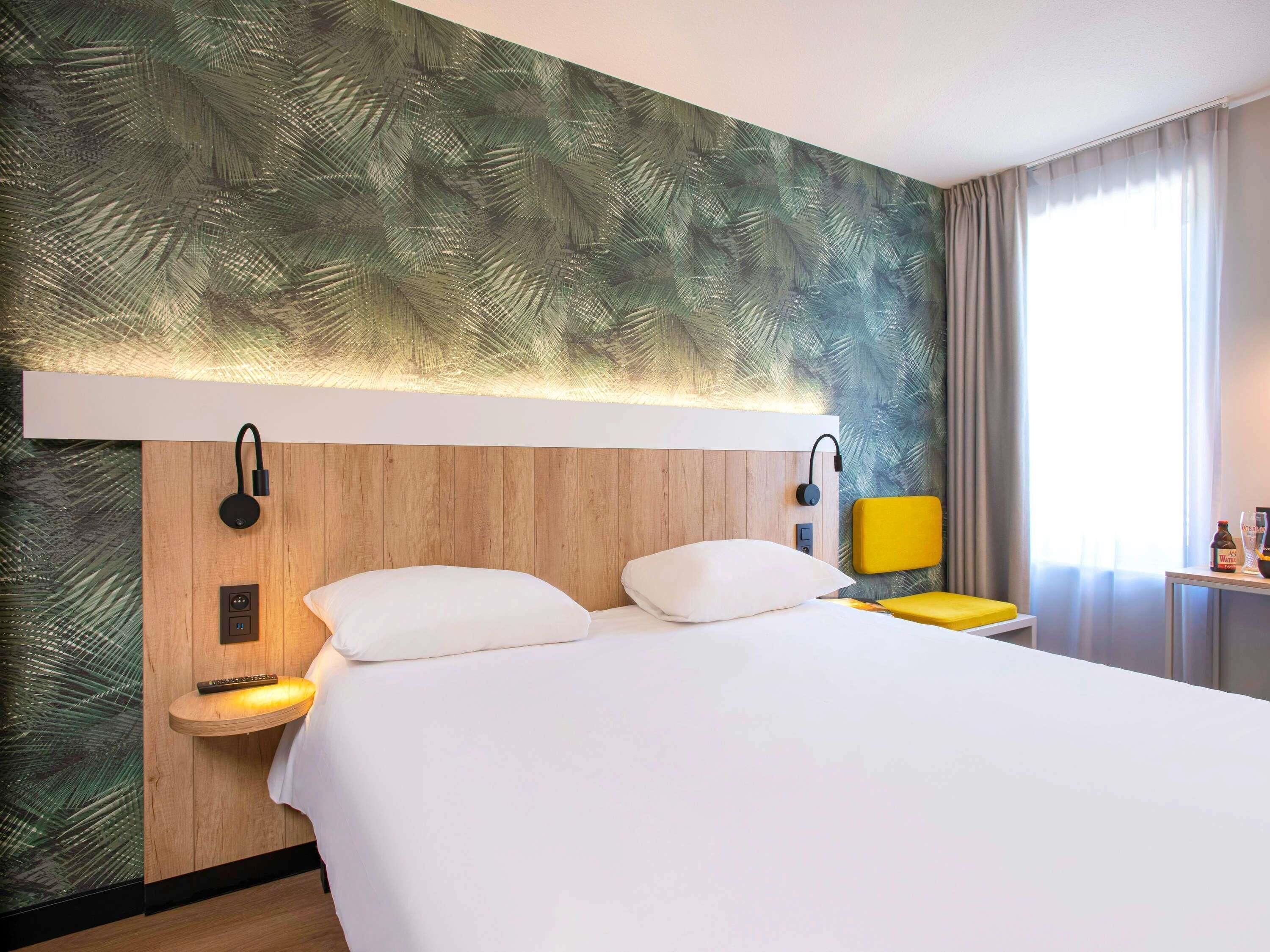Ein Hotelzimmer mit Bett, Nachttischen, einer Lampe und Blick ins Freie.