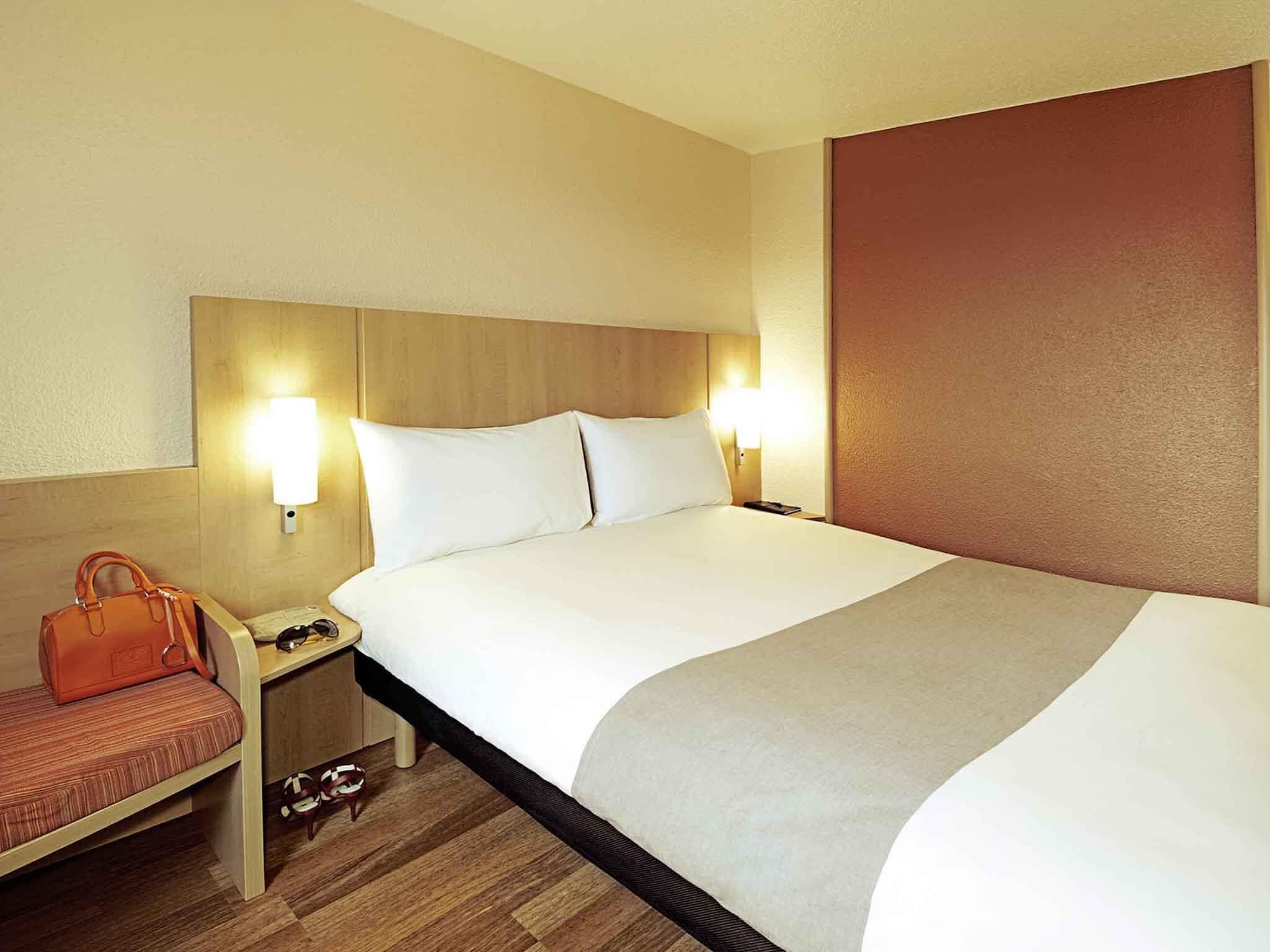 A hotel room with a large bed, bedside tables, a nightstand, a lamp, a handbag, and a pair of shoes.