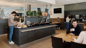 A modern cafe with a counter, seating area, and a TV mounted on the wall. - ibis Brussels Waterloo (Waterloo)