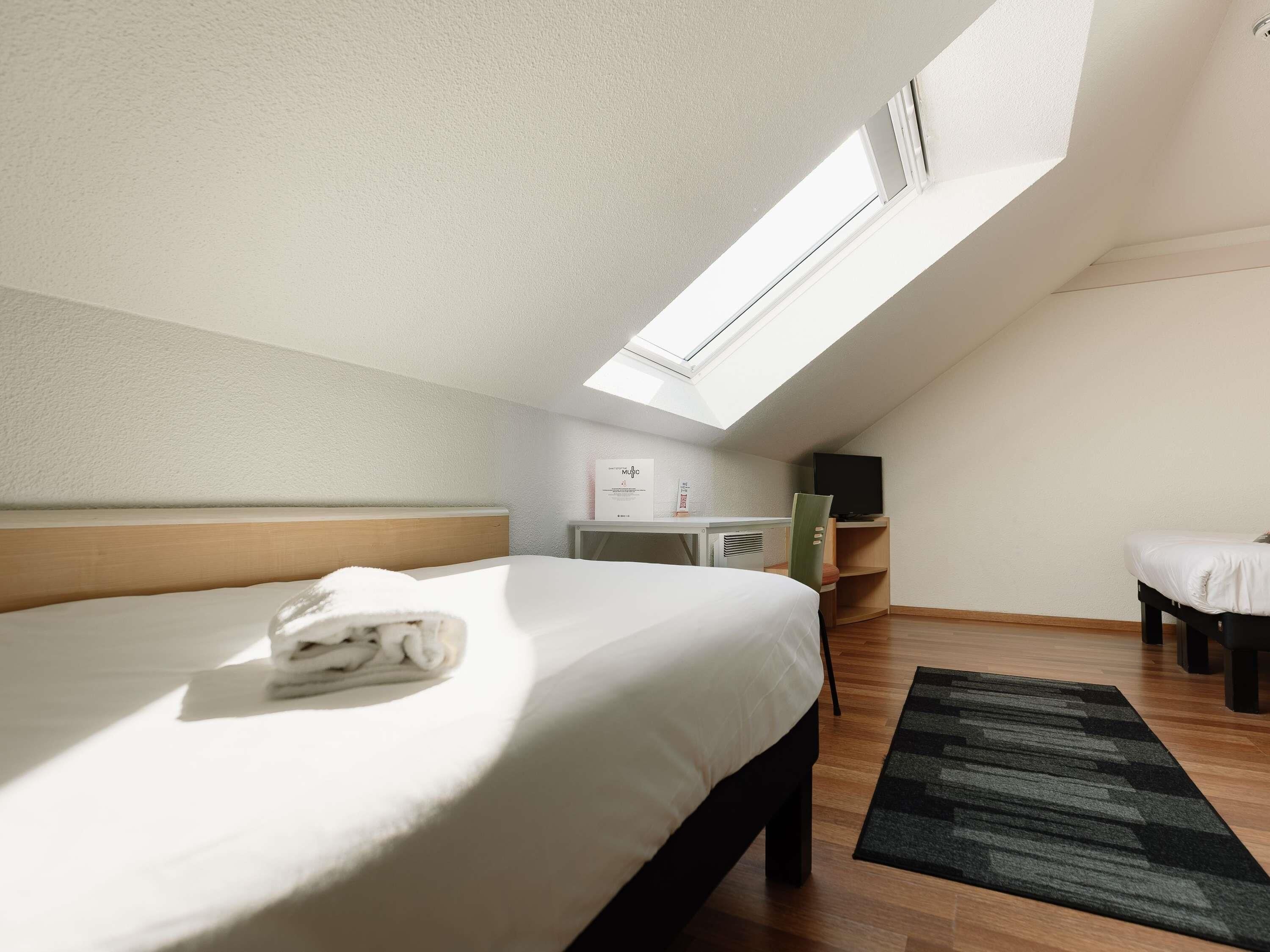 A bedroom with a skylight, a bed, a desk, a chair, and a TV.