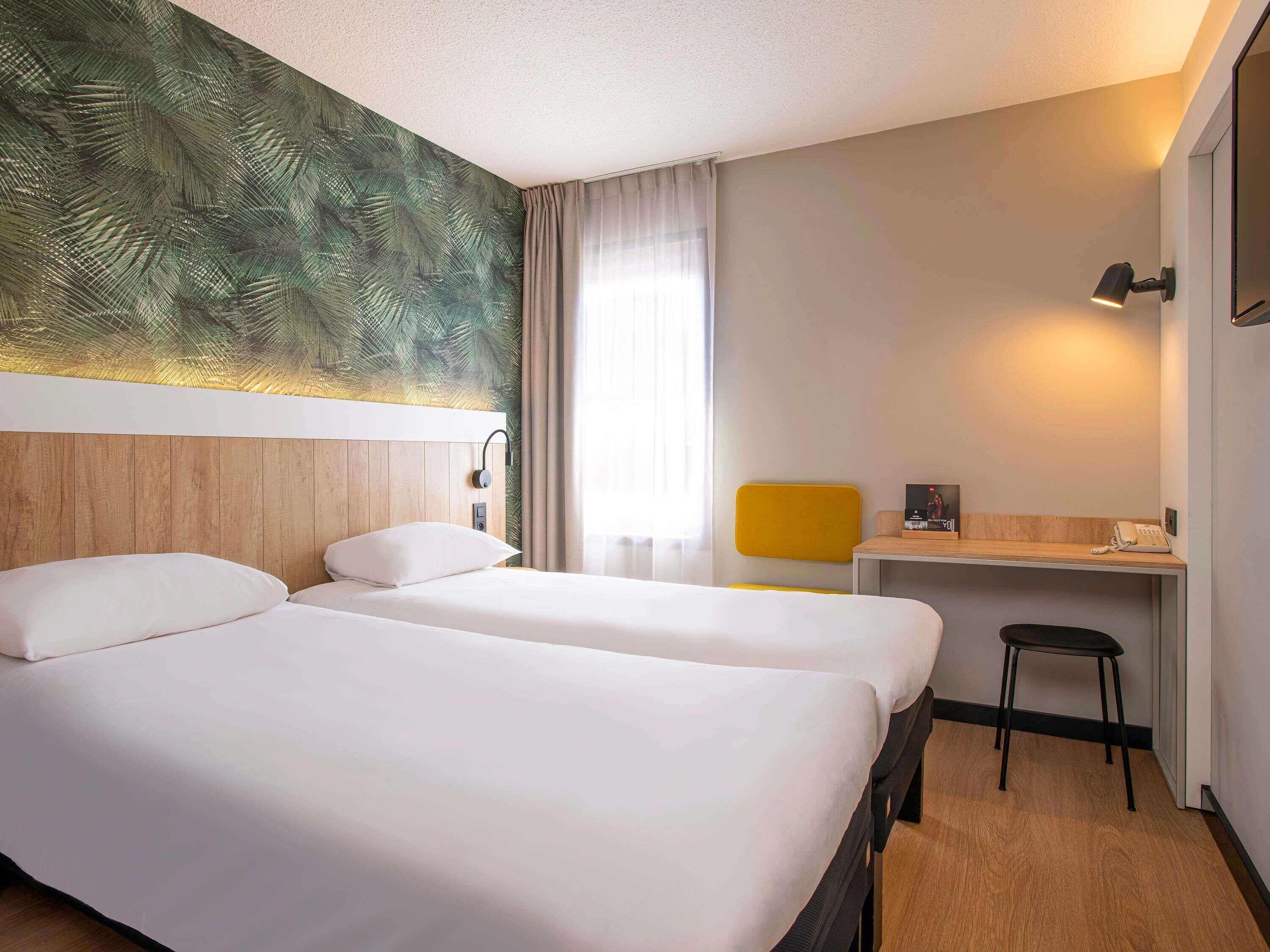 Habitación de hotel con dos camas, un escritorio, una silla, un teléfono y una pared con diseño de hojas.