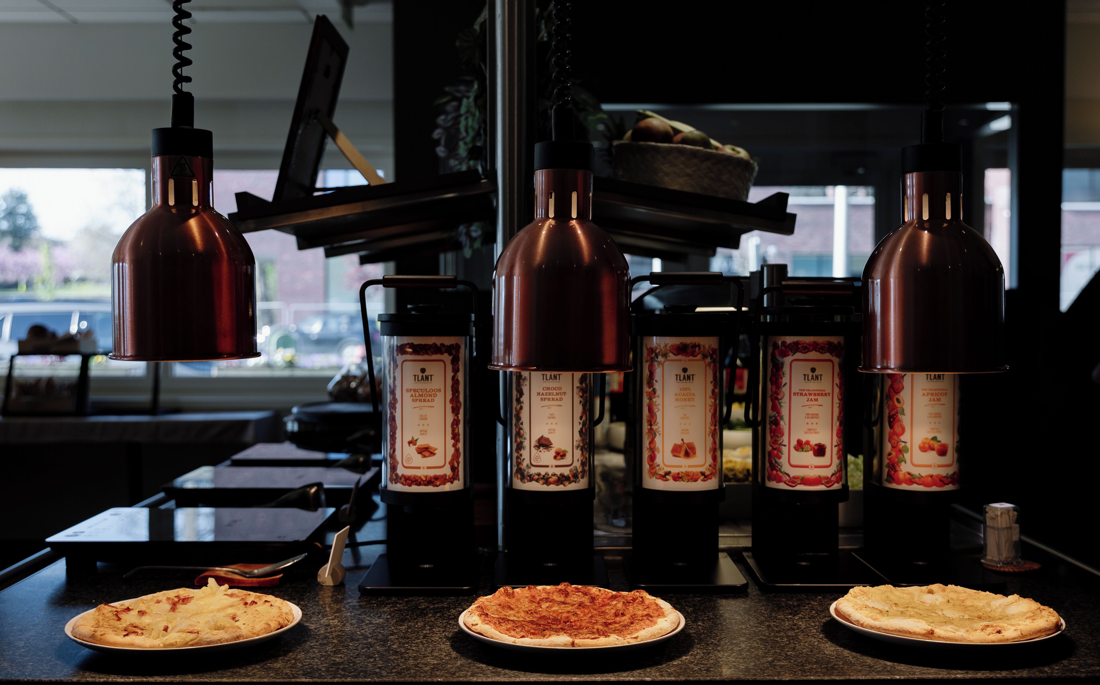 En køkkenbordplade med tre pizzaer, en kaffemaskine og hængende kobberlamper i køkkenet.