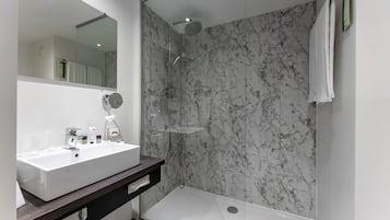 A modern bathroom with a marble shower wall, a white sink, and a large mirror.