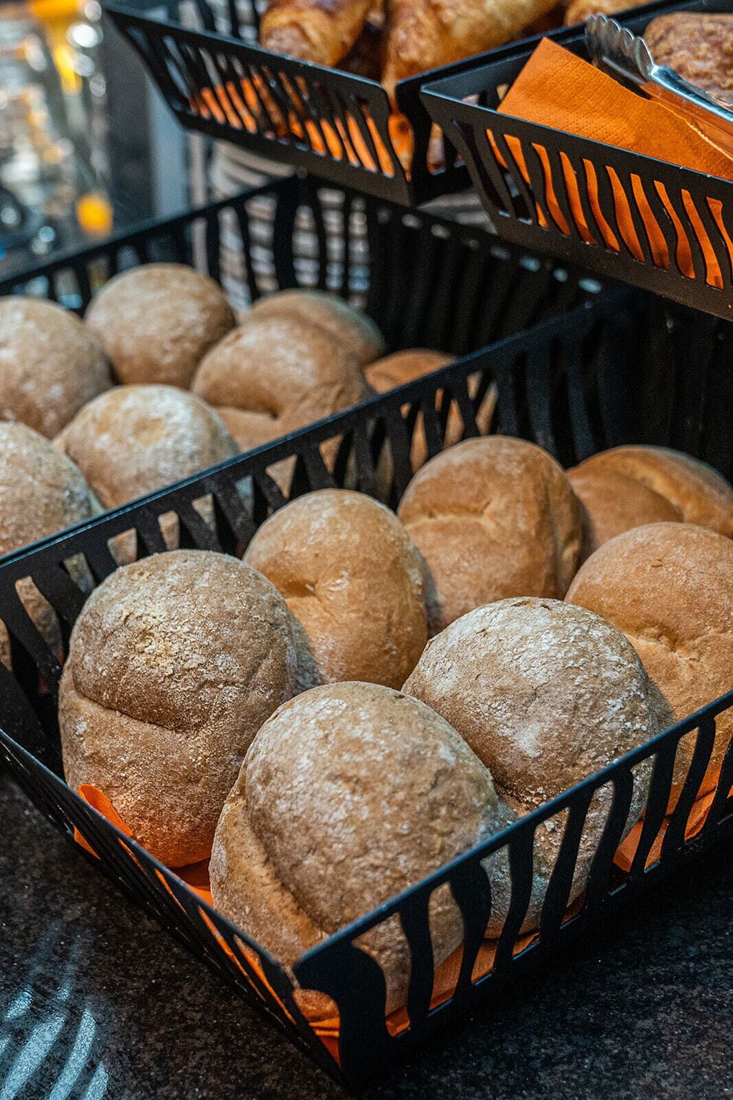 A tray of round, dusted bread rolls in a black basket.