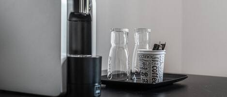 A coffee machine with a tray holding two glasses and a canister with coffee-related words.