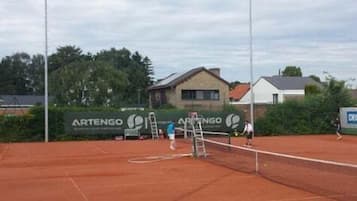 Ein Tennisplatz mit Netz, umgeben von Wohnhäusern und einem Banner mit dem Text "ARTENGO".