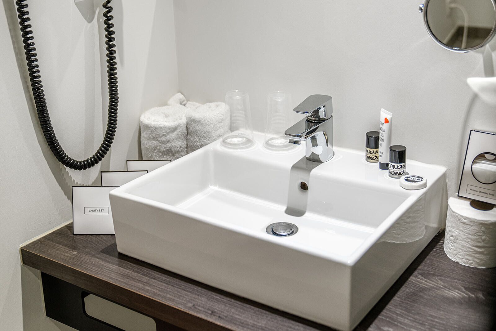 Un lavabo blanc dans la salle de bain, avec un robinet chromé, un miroir et des articles de toilette posés sur le comptoir.