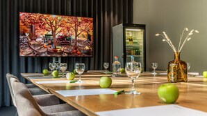 A conference room with a long table, chairs, a television, and a minibar. - Velotel Brugge (Bruges)