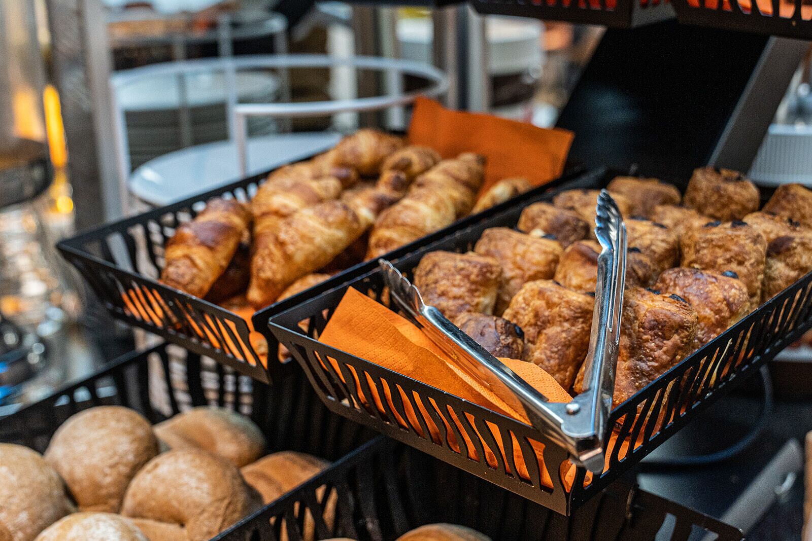 Trays of baked goods, including croissants and muffins, displayed in a bakery setting.