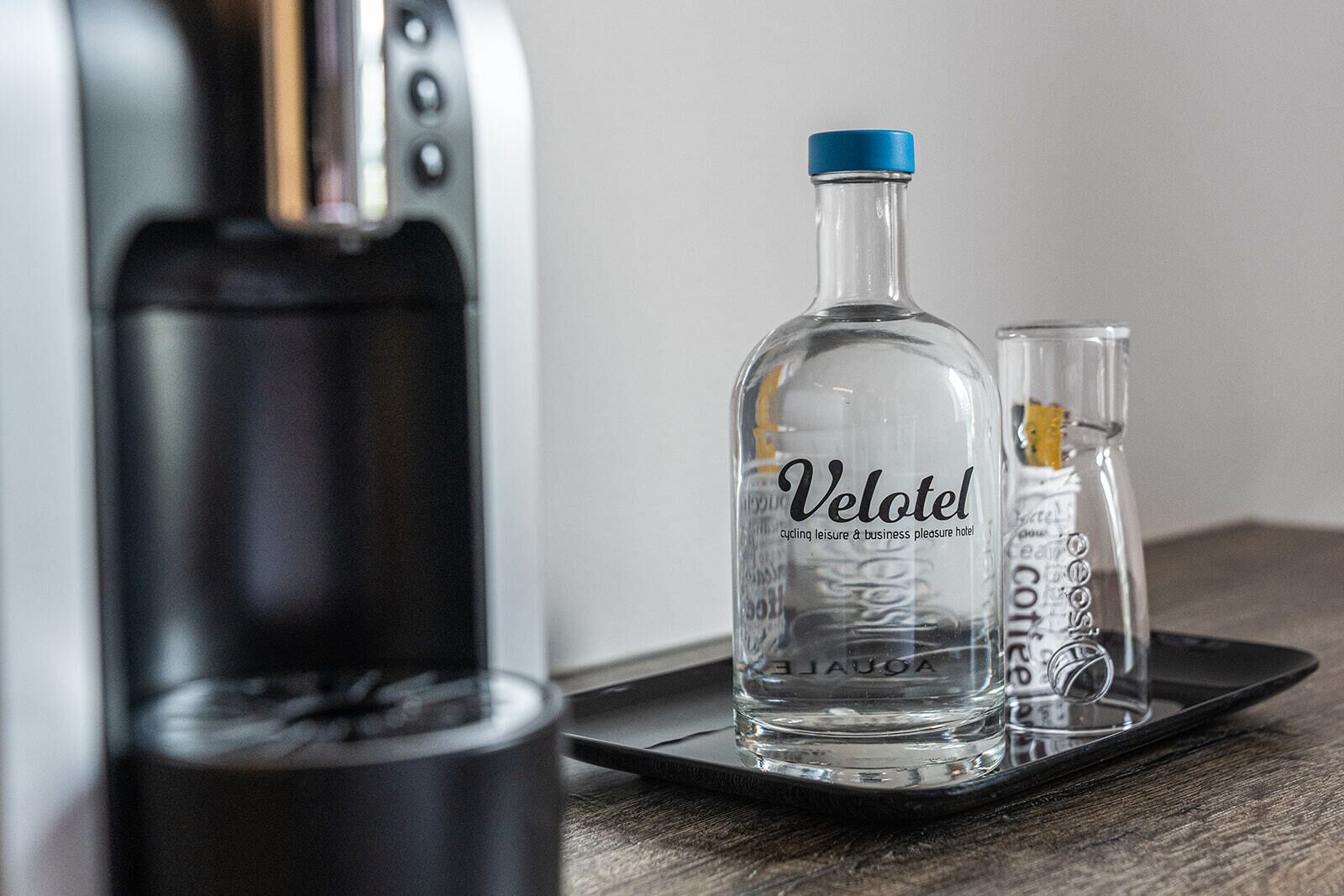 A water dispenser, a bottle labeled "Velotel," and a glass on a tray.