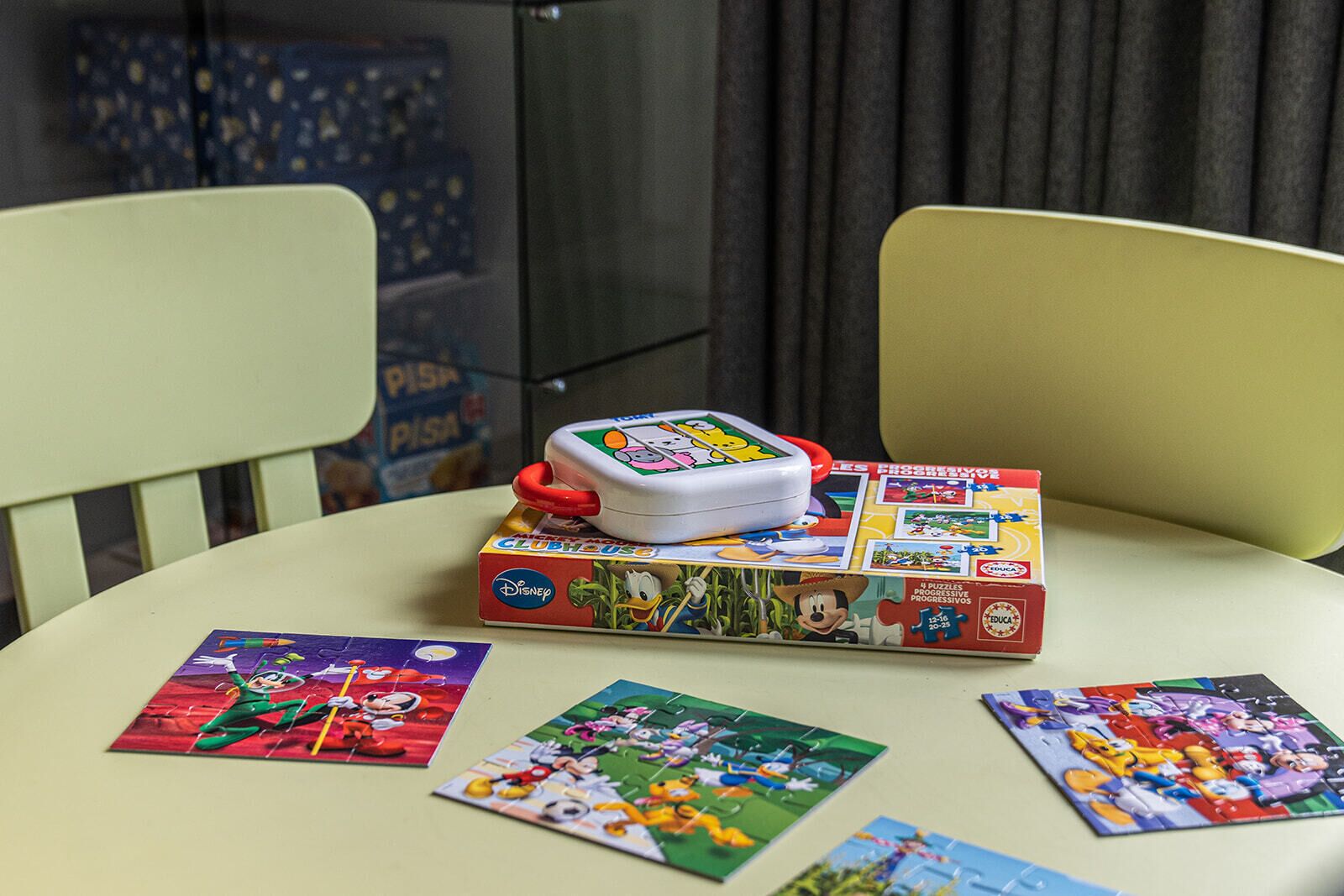 Una mesa con una caja de juego de mesa y sus piezas, sillas y una cortina al fondo.