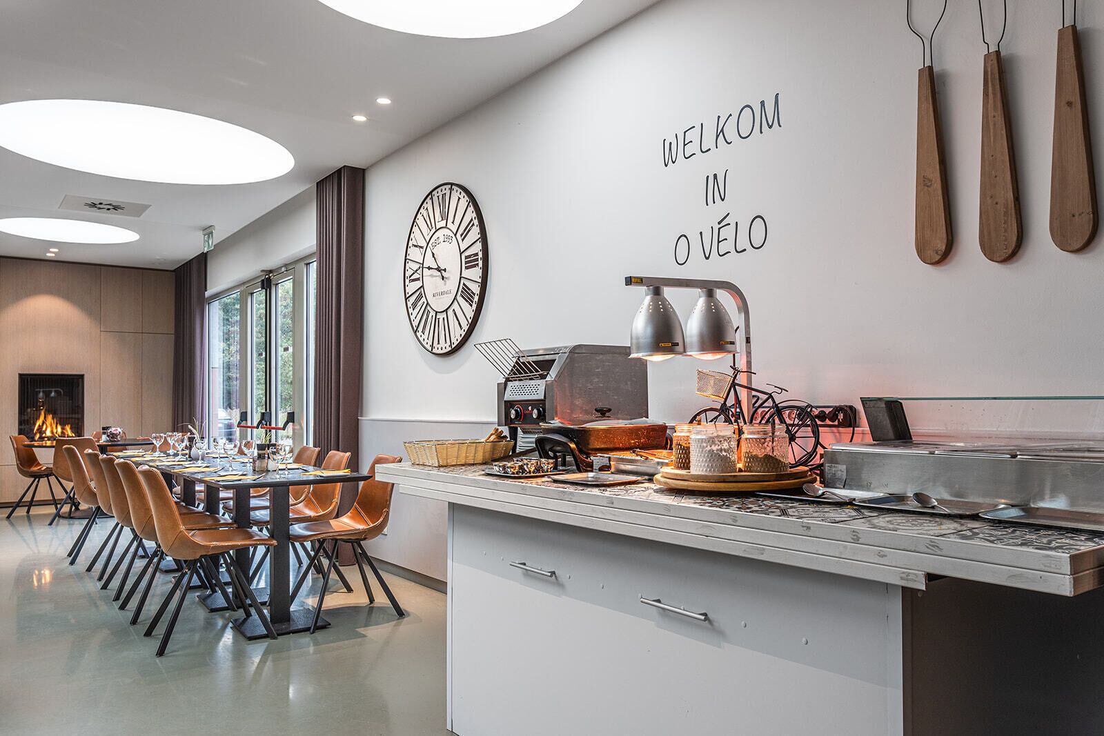 A modern kitchen with a dining area, a large clock, and a welcome sign.