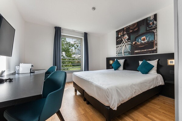 A modern hotel room with a bed, a desk, and a large window.