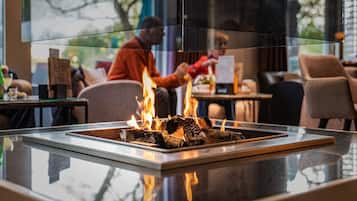 A glass-top table with a fire feature in the center, surrounded by chairs and tables in a modern indoor setting.