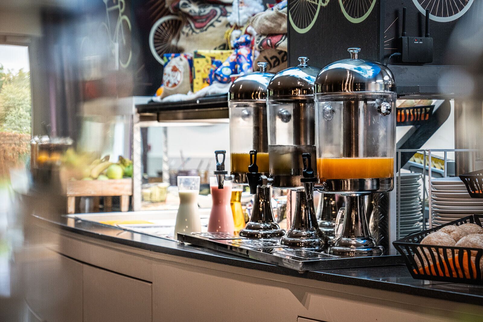 A coffee station with multiple dispensers, a milk pitcher, and a basket of pastries.