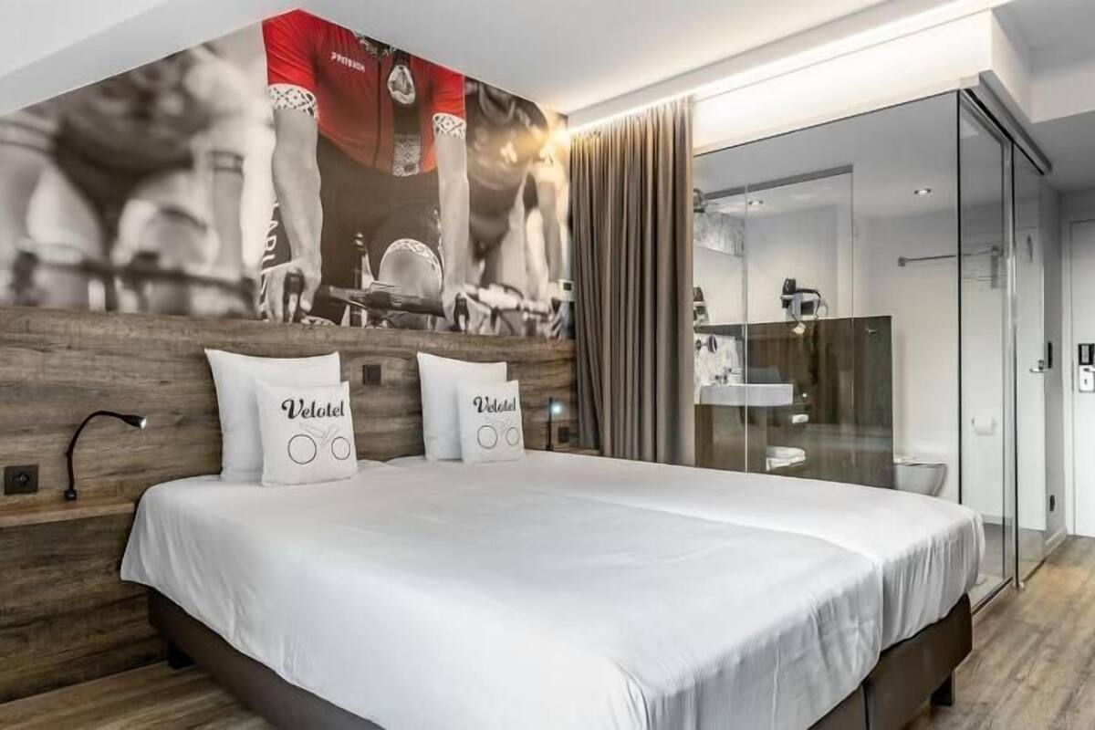 A modern hotel room with a large bed, wooden headboard, and a wall-mounted artwork.