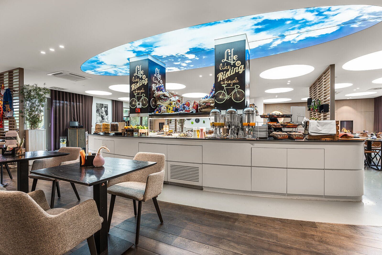 Un café moderne doté d’un comptoir central, d’un espace salon et d’un plafond décoré pour évoquer le ciel.