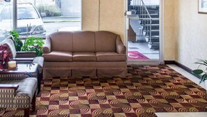 Um hall com carpete estampado, um sofá, uma poltrona e uma televisão na parede.