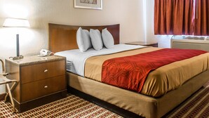 Quarto de hotel com cama, mesa de cabeceira, abajur, quadro na parede e janela com cortinas.