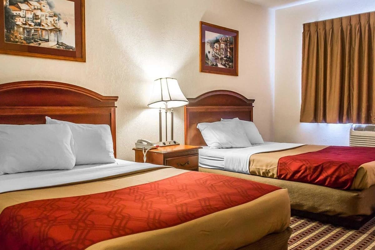 Une chambre d’hôtel avec deux lits, une table de chevet avec une lampe et deux tableaux encadrés au mur.
